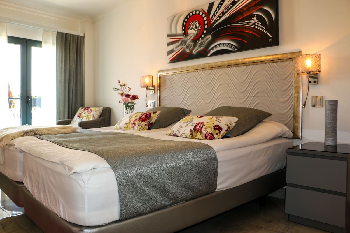 Un lit double avec des coussins à motifs floraux, une tête de lit à motif chevrons et une table de chevet avec une lampe.