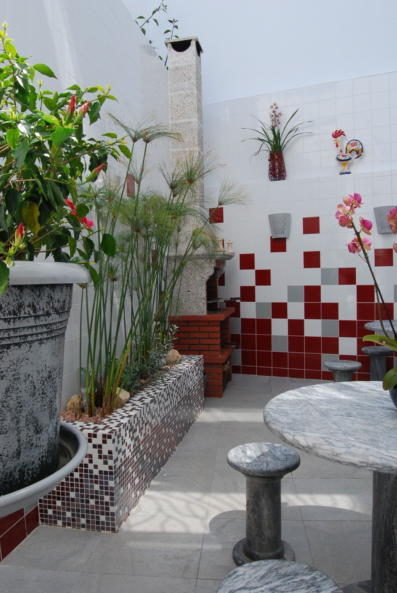 A patio area with a tiled wall, a stone planter, a round table, and a seating bench.