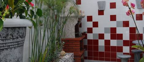 A patio area with a tiled wall, a stone planter, a round table, and a seating bench.