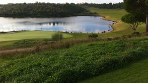 Un parcours de golf avec un étang, des arbres et un ciel dégagé.