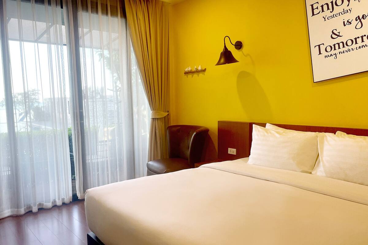 Een hotelkamer met een bed, een stoel, een wandlamp en een raam met gordijnen.
