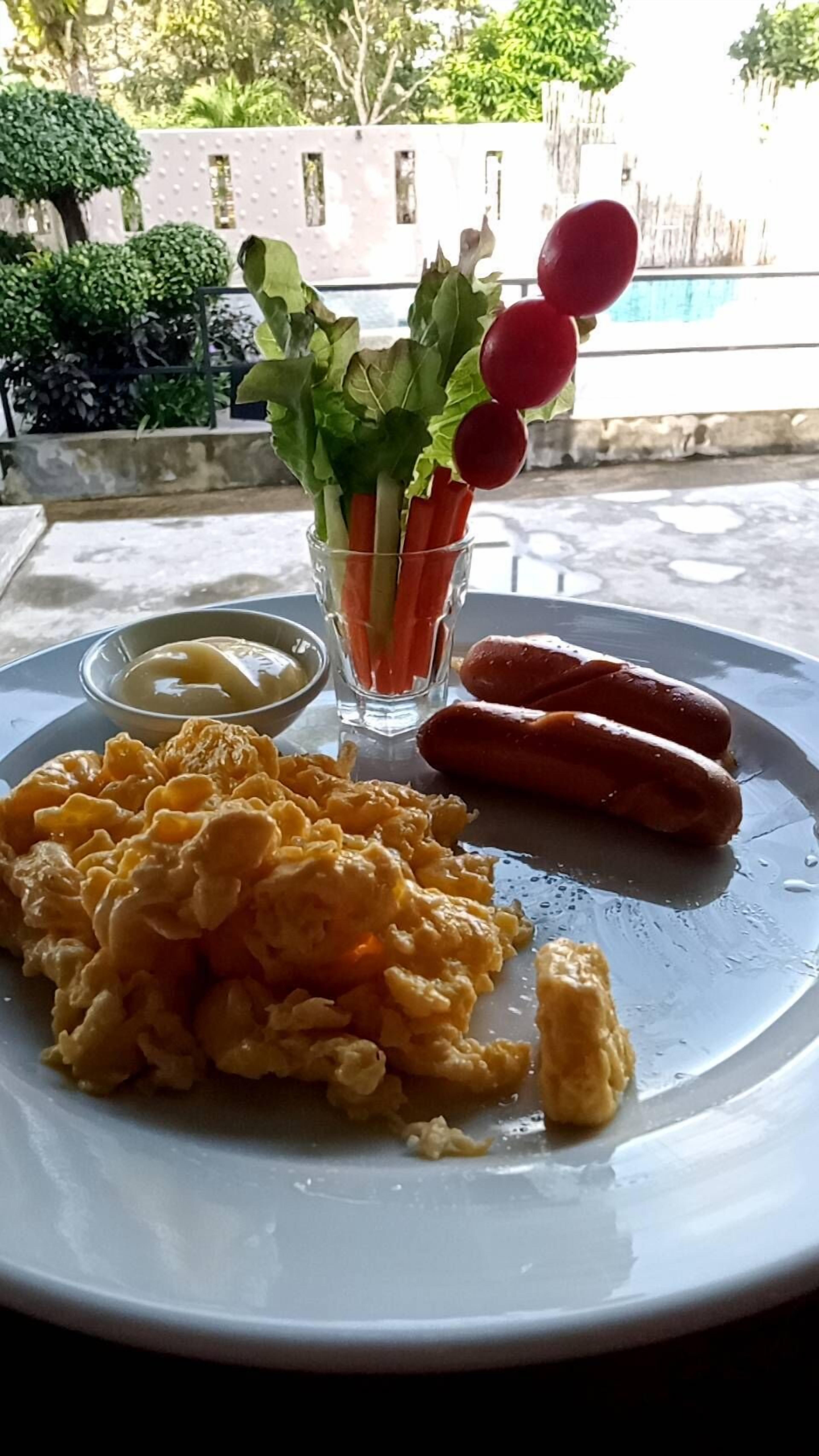 A plate with scrambled eggs, sausages, and a small salad with radishes and lettuce.