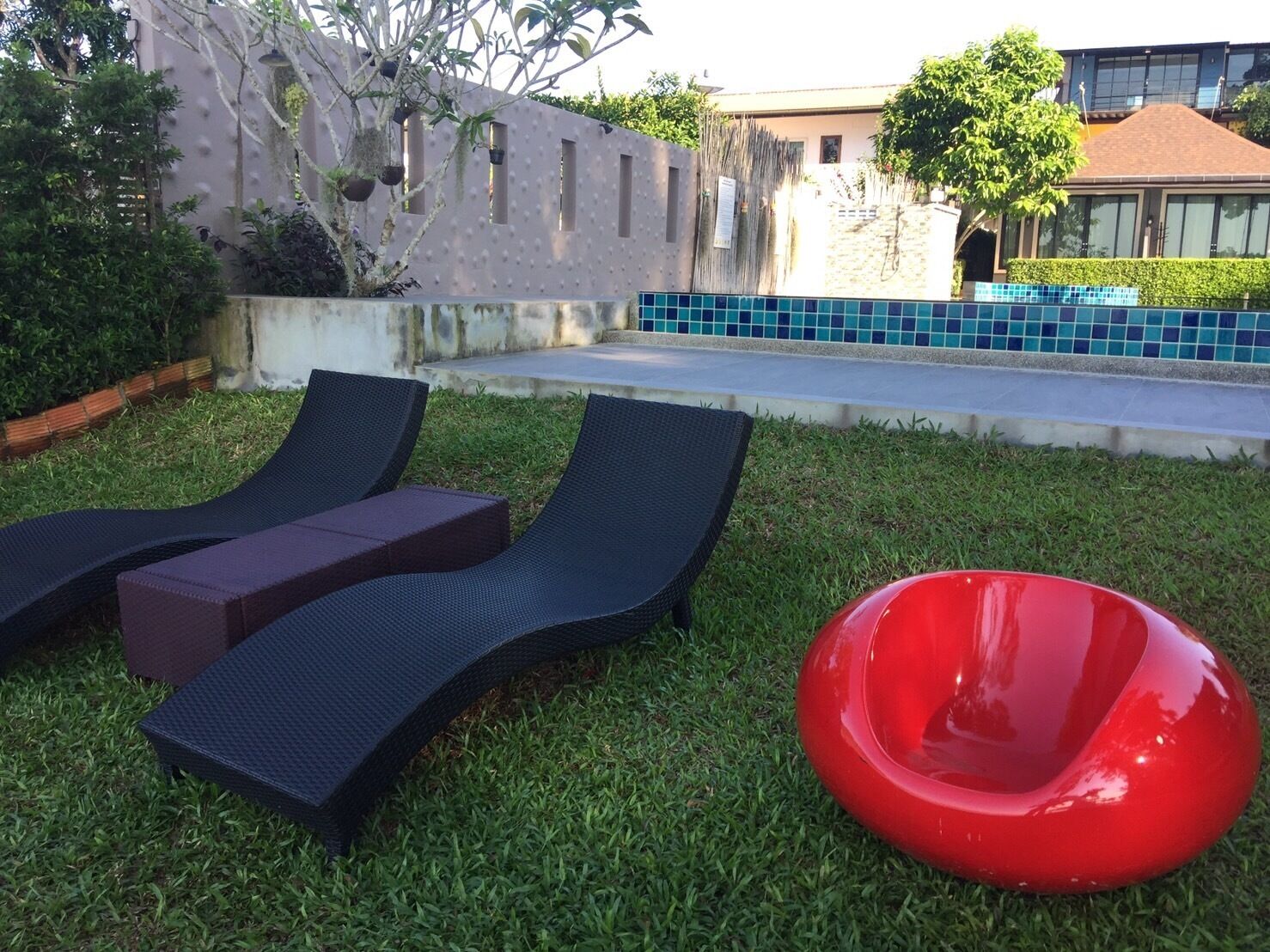 Un espace extérieur verdoyant avec deux fauteuils de jardin aux couleurs sombres et un objet sphérique rouge.