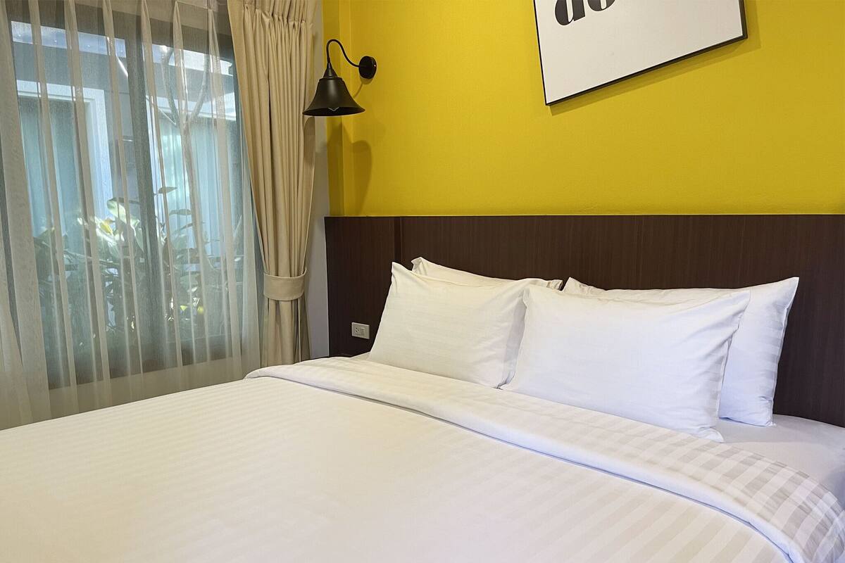 Een hotelkamer met een groot bed, een hoofdbord, een wandlamp en een raam met gordijnen.