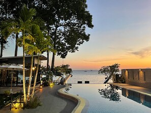 A poolside area with a curved pathway leading to a pool, surrounded by palm trees and a view of the sea at sunset. - Blue Orchid Beach Krabi (Krabi)