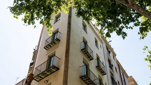 A multi-story building with balconies, large windows, and a tree in the foreground. - Studio 2 pax in Born (Barcelona)
