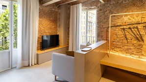 A modern living room with a stone wall, a flat-screen TV, a white sofa, and a large window with curtains. - Studio 2 pax in Born (Barcelona)