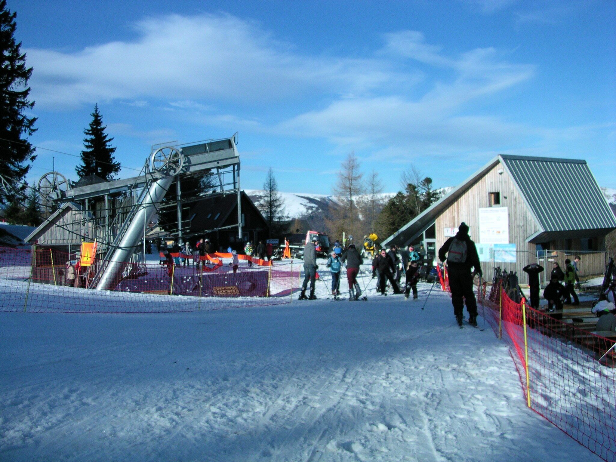 Ein Skigebiet mit Skilift, einem Holzbau und einem eingezäunten Bereich.