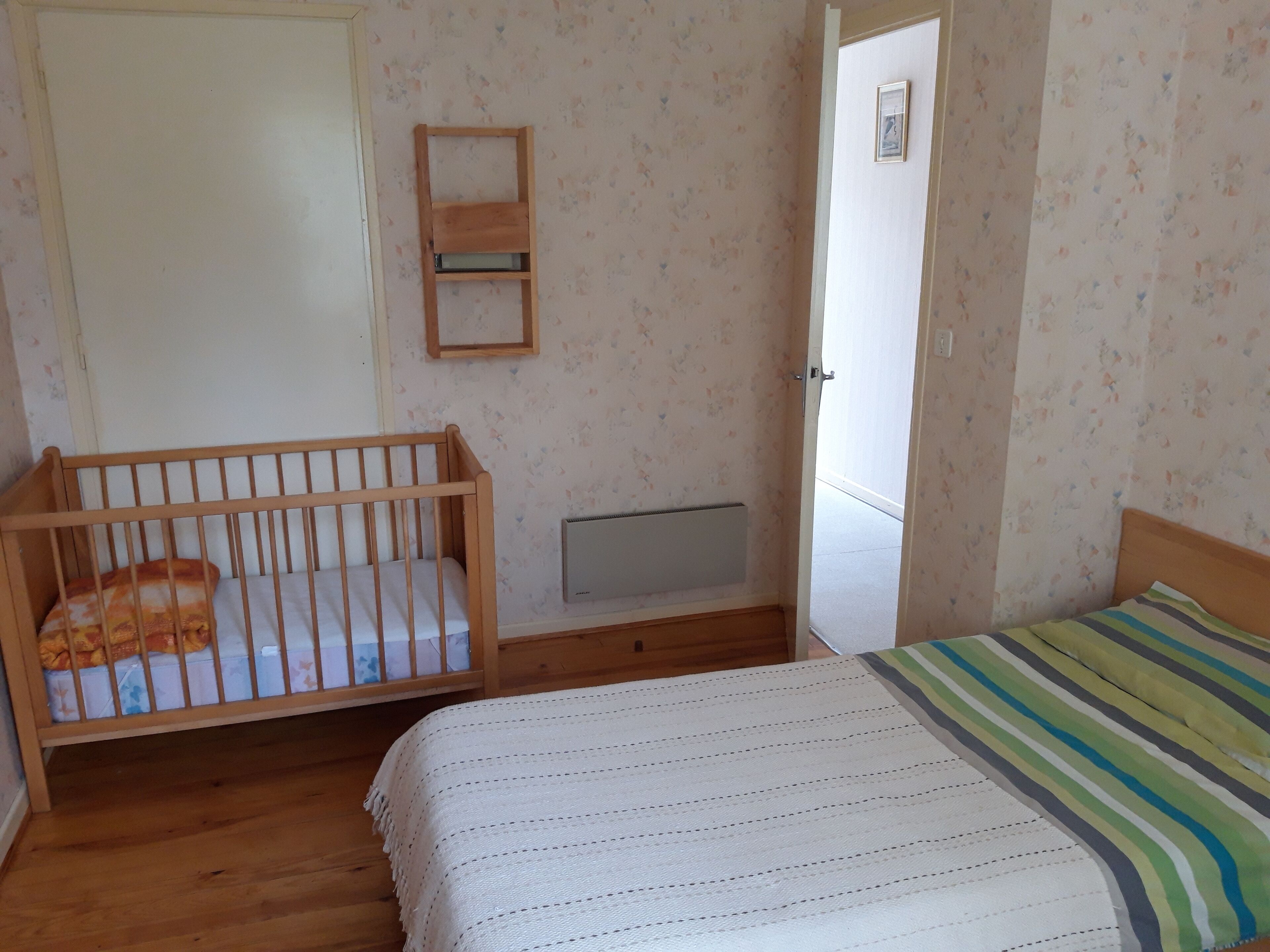 A bedroom with a wooden crib, a bed with a striped blanket, a radiator, and a door leading to another room.