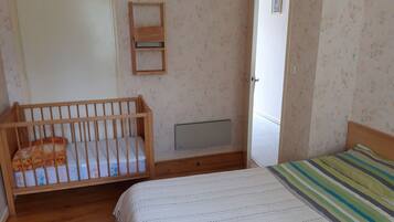 A bedroom with a wooden crib, a bed with a striped blanket, a radiator, and a door leading to another room.