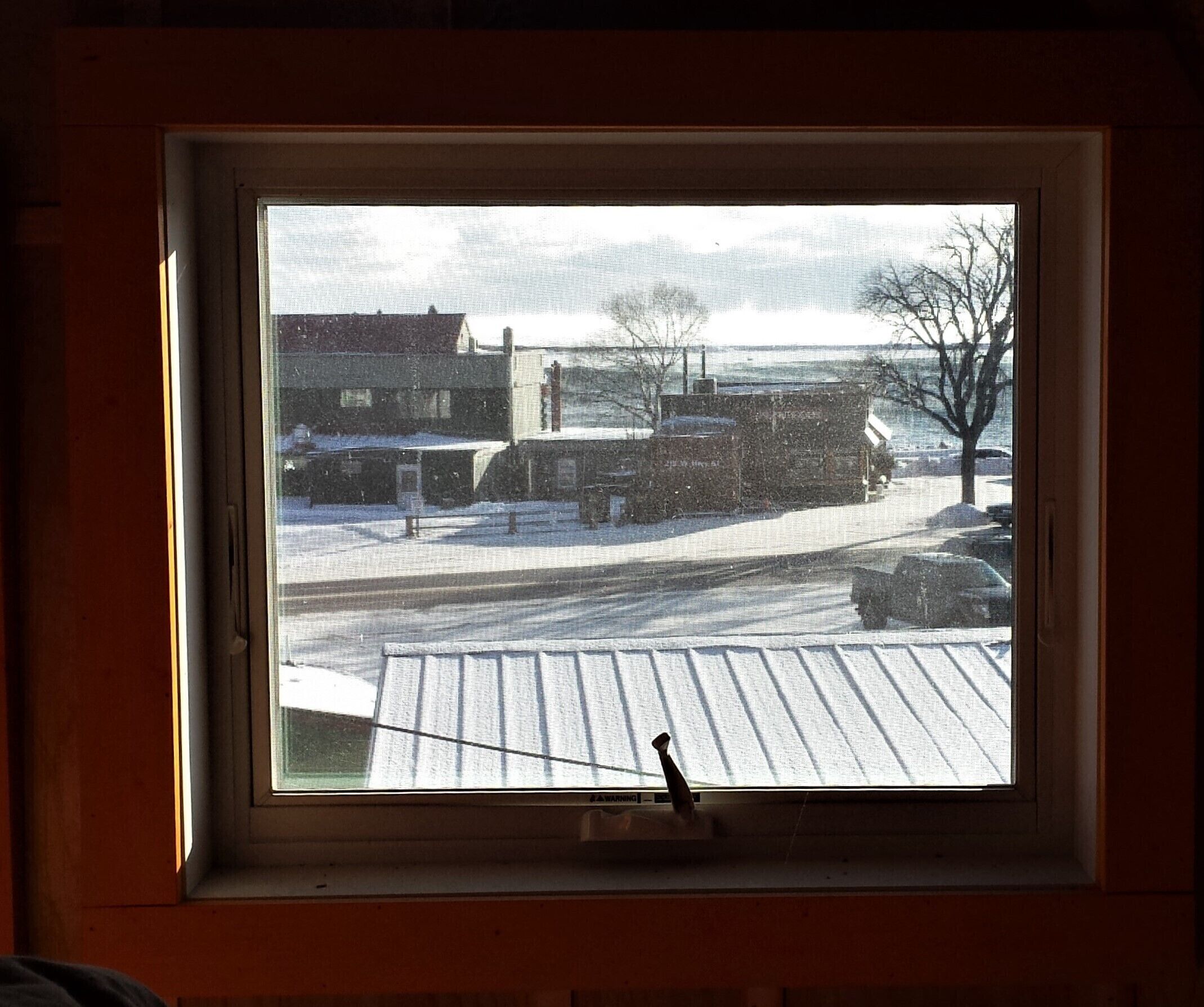 A window with a view of a snowy street, a parked truck, and a building in the background.