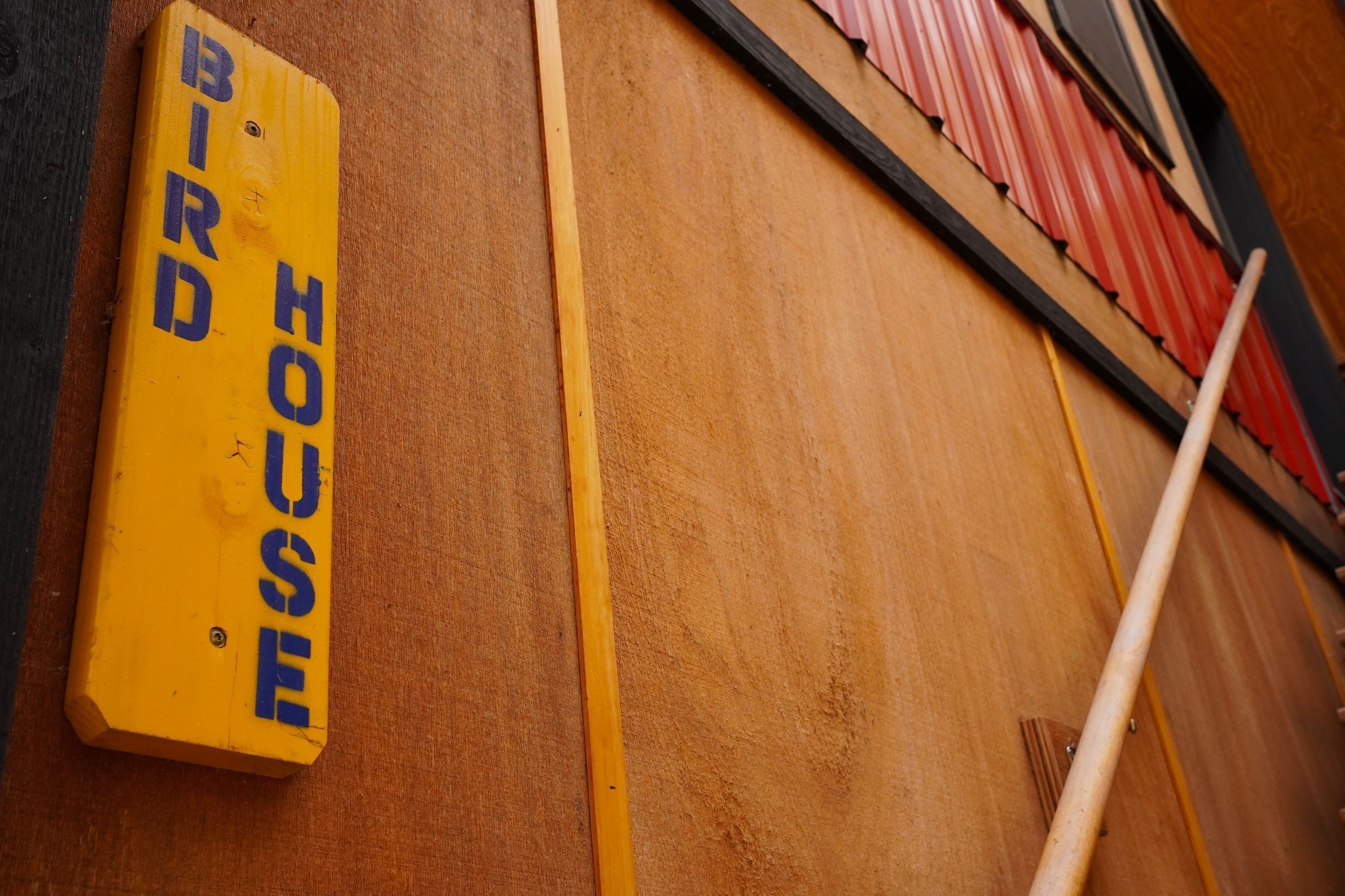 A wooden wall with a yellow sign that reads "BIRD HOUSE".