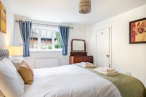 A bedroom with a bed, a dresser, a window with curtains, a radiator, and a painting on the wall.