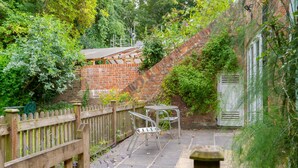 Un espace jardin agrémenté d’un mur en briques, d’une clôture en bois et d’un ensemble de table et de chaises en métal.
