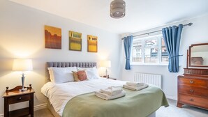 Una habitación de hotel con cama, mesitas de noche, cómoda, ventana con cortinas y una obra de arte en la pared.