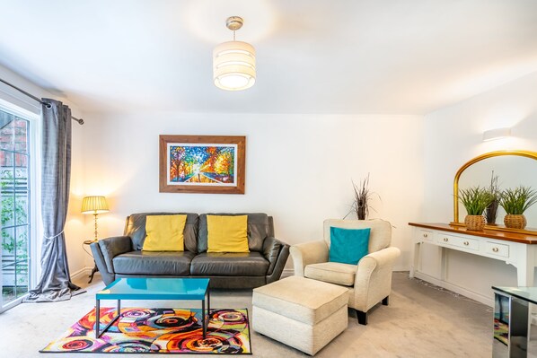 A living room with a sofa, ottoman, coffee table, and a painting on the wall.