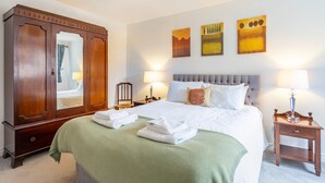 Une chambre d’hôtel avec un grand lit, une armoire, deux tables de chevet avec des lampes et trois tableaux accrochés au mur.