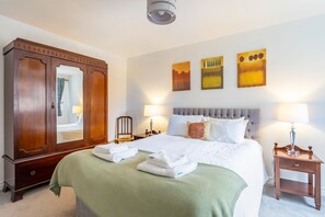 Una habitación de hotel con una cama grande, un armario, dos mesitas de noche con lámparas y tres cuadros colgados en la pared.