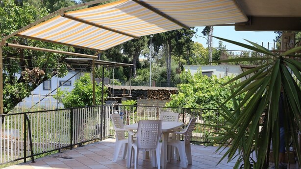 An outdoor patio with a table and chairs, a striped canopy, and a view of surrounding greenery and buildings. - La Casa dell'Orso (Ciampino)