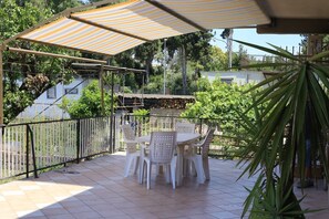 An outdoor patio with a table and chairs, a striped canopy, and a view of surrounding greenery and buildings. - La Casa dell'Orso (Ciampino)