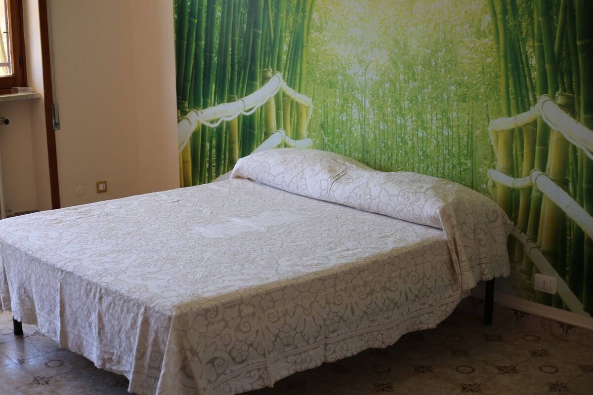 A single bed with a white bedspread in a room with a bamboo curtain backdrop.