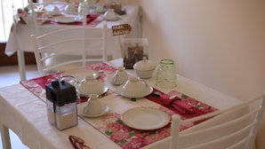 A dining table set with white plates, bowls, and glasses, with a floral tablecloth. - La Casa dell'Orso (Ciampino)