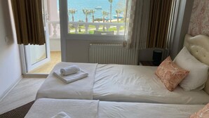 Habitación de hotel con dos camas, vista al mar y un balcón con barandilla.