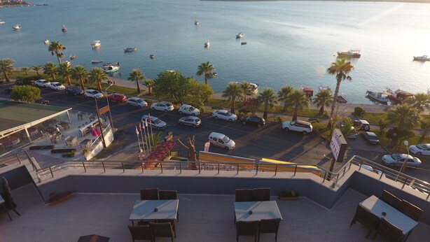 Vista al mar desde una terraza con mobiliario exterior, zona de estacionamiento y barcos en el agua.