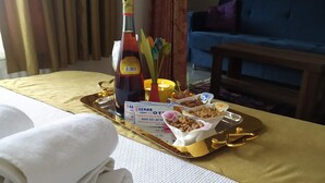 Habitación de hotel con una mesa ordenada que presenta una botella, una bandeja con aperitivos y un cartel con detalles de la habitación.