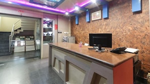 A reception area with a marble wall, a reception desk, a computer, and a fire exit sign. - Hotel Nirmala Residency (Bhubaneshwar)