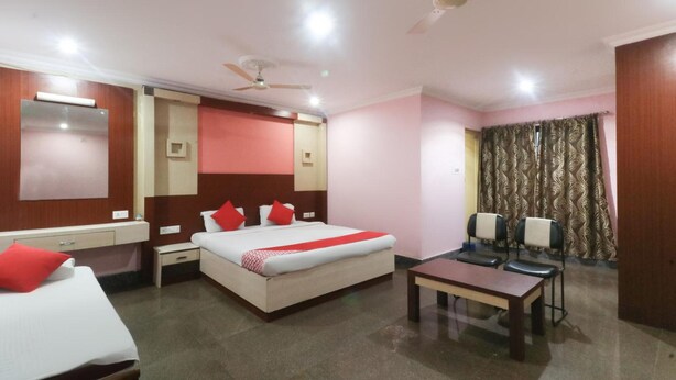 A hotel room with a bed, bedside tables, a desk, and a ceiling fan. - Hotel Nirmala Residency (Bhubaneshwar)