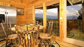 A wooden cabin with a dining area featuring a round table and chairs, a refrigerator, and a view through a glass door.