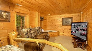 A wooden cabin interior with a couch, a television displaying a racing scene, and a window with blinds.