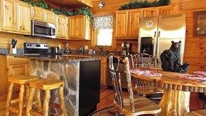 A rustic cabin-style kitchen with wooden cabinets, a stone island, and a bear statue.
