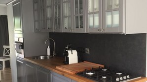 Une cuisine moderne avec des meubles gris, un plan de travail en bois, une cuisinière à gaz et une poubelle noire.