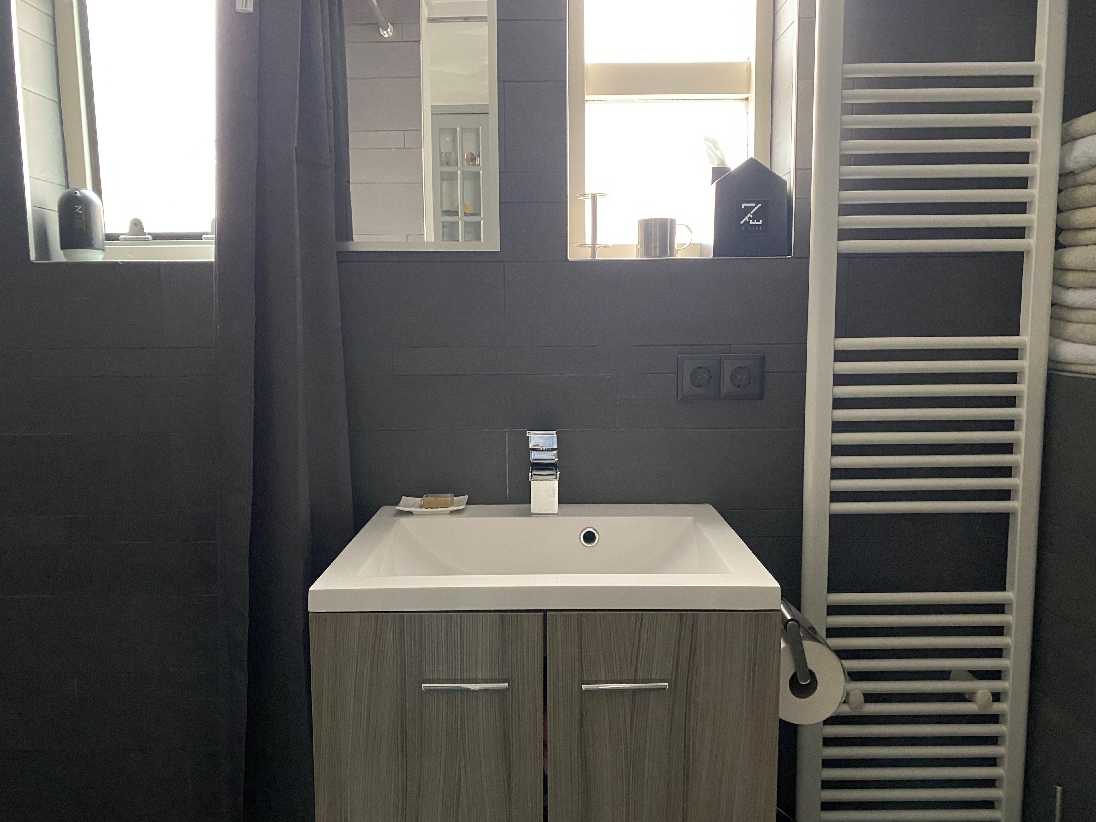 Un baño con lavamanos blanco, armarios de madera, un perchero y un espejo.