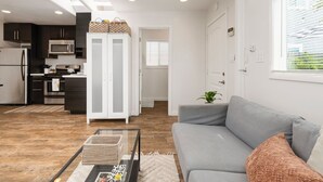 Una cocina moderna con armarios oscuros, un refrigerador blanco y un microondas. Hay un sofá gris con un cojín y una pequeña planta en la sala de estar.