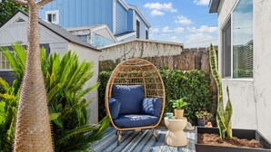 Una casa azul con una hamaca colgante, una palmera y plantas en macetas.
