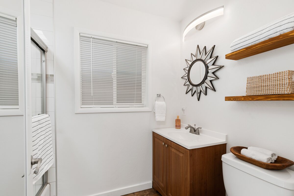 Un baño moderno con un lavabo blanco, un mueble de madera, un inodoro y un espejo con forma de sol.