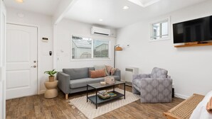 Una sala de estar moderna con un sofá gris, una mesita de centro, un sillón estampado y un televisor de pantalla plana montado en la pared.
