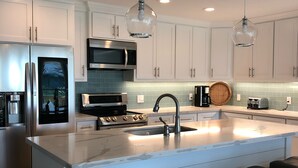 Une cuisine moderne avec des meubles blancs, des appareils en acier inoxydable, un grand îlot central doté de tabourets et un éclairage suspendu.