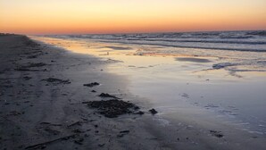Une plage au coucher du soleil, avec des vagues calmes et des débris éparpillés sur le sable.