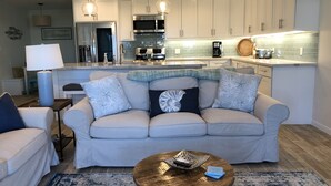 Un salon moderne avec un canapé beige, une table basse et une cuisine en arrière-plan.