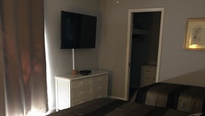 A bedroom with a bed, a ceiling fan, a dresser, a television, and a door leading to another room.