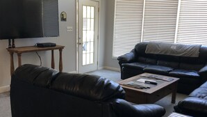 A living room with a black leather sofa, a wooden coffee table, a television on a stand, and a ceiling fan.