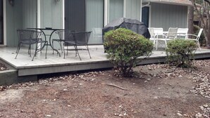 A covered patio with metal chairs and a table, a small covered grill, and a door with a window.