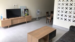 A modern living room with a flat-screen TV, wooden entertainment unit, and a dining area with a table and chairs.