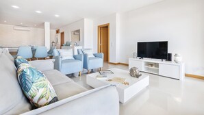 A modern living room with a sofa, chairs, a coffee table, and a TV. - Flat Downtown OCV - 5min Beach (Albufeira)