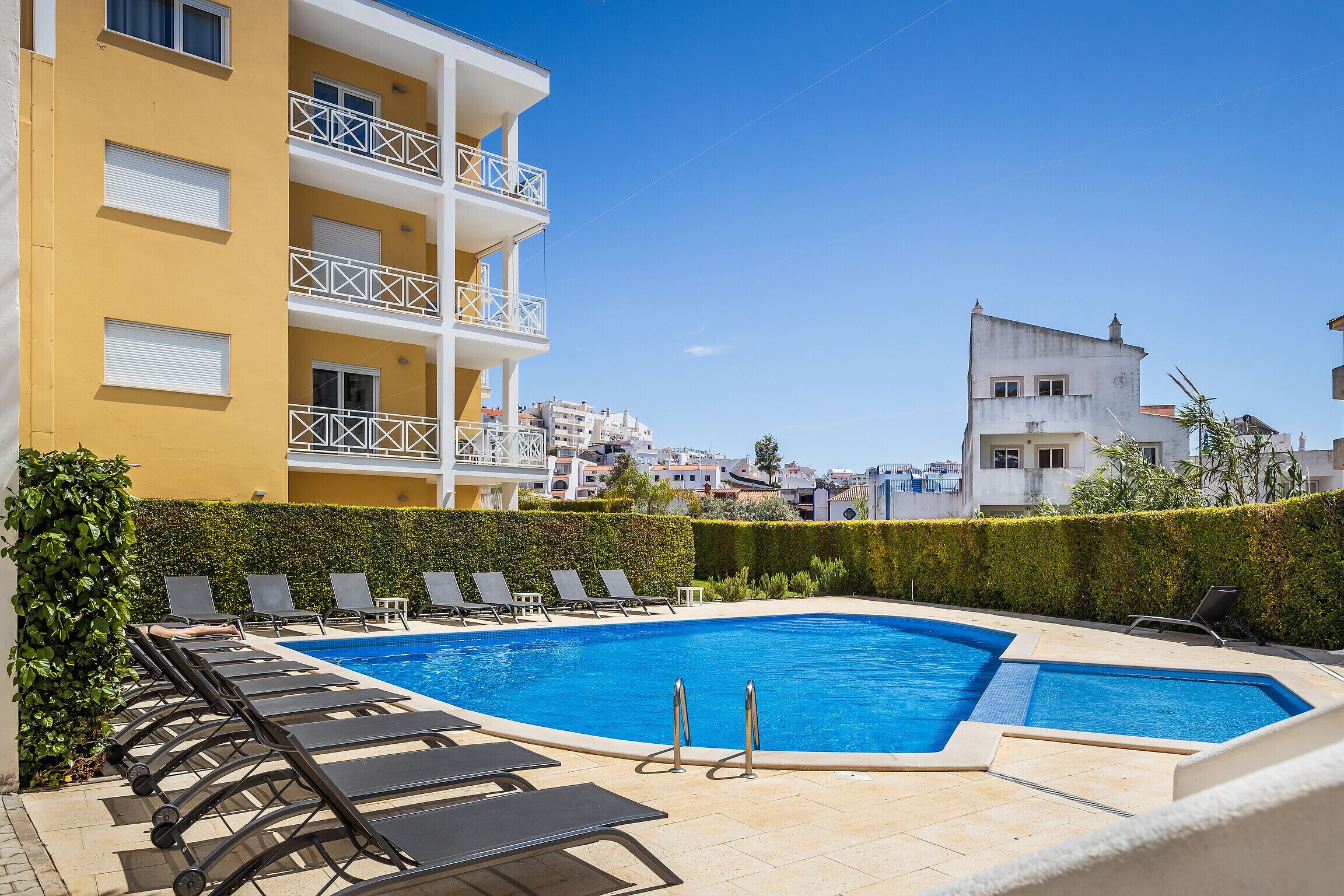 A swimming pool with lounge chairs and a building with balconies.