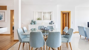 A modern dining area with a glass table and light blue upholstered chairs. - Flat Downtown OCV - 5min Beach (Albufeira)